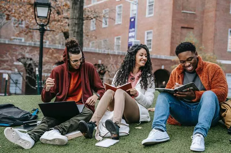 Three students sitting outdoors on campus sharing notes